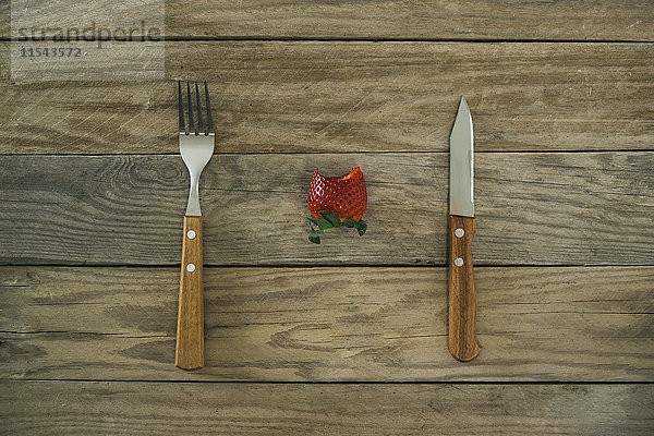 Gabel,  Messer und eine gebissene Erdbeere auf Holz
