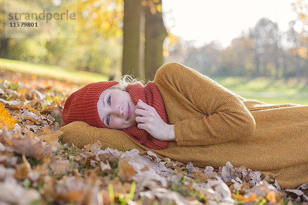 Hübsche blonde Frau im Park im Herbst lächelnd vor der Kamera liegend