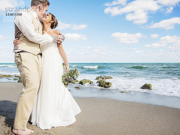Kaukasische Braut und Bräutigam umarmen sich am Strand
