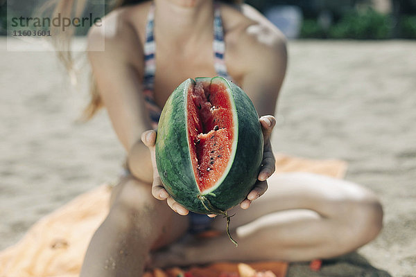 Kaukasische Frau zeigt aufgeschnittene Wassermelone am Strand