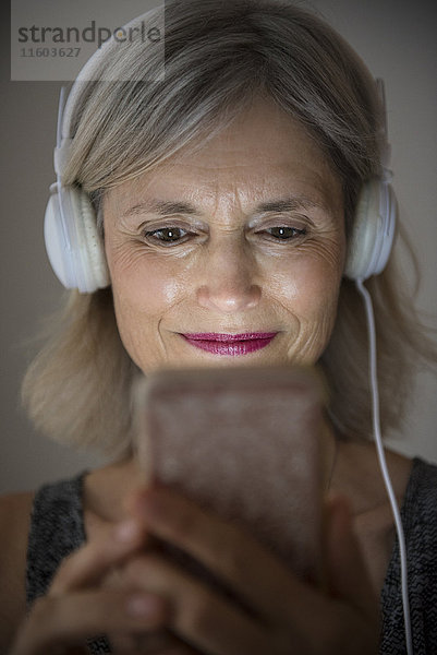 Lächelnde kaukasische Frau,  die mit ihrem Mobiltelefon Musik hört