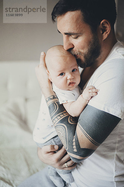 Kaukasischer Vater mit Tätowierungen auf den Armen,  der seinen kleinen Sohn küsst