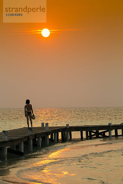 Gemischtrassige Frau steht auf einem Dock bei Sonnenuntergang