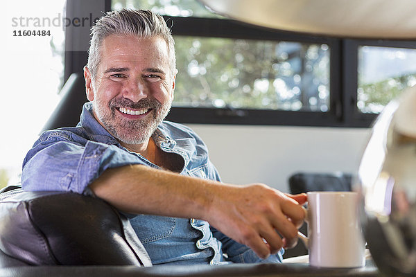 Kaukasischer Mann sitzt auf dem Sofa und trinkt Kaffee