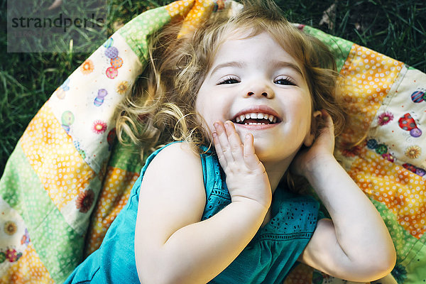 Porträt eines lächelnden kaukasischen Mädchens im Vorschulalter,  das auf einer Decke im Freien liegt