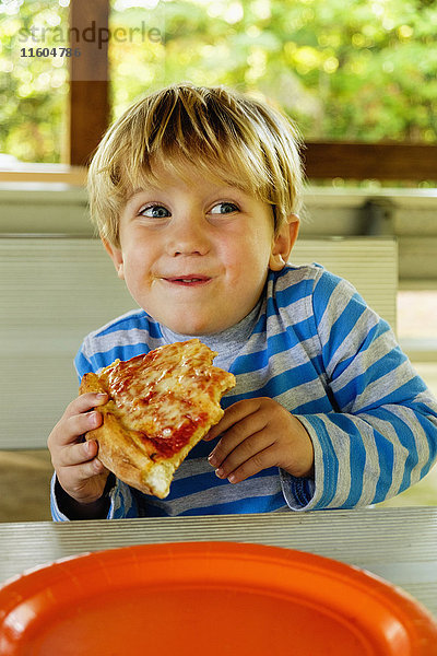 Verspielter kaukasischer Junge isst Pizzastück