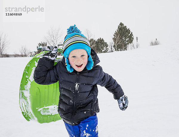 Lächelnder Junge läuft mit Schlitten im Winter