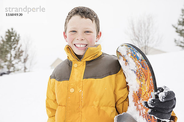 Lächelnder Junge posiert mit Snowboard im Winter