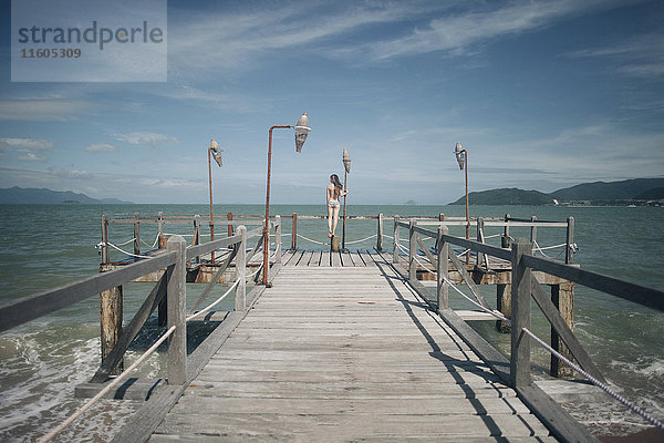 Kaukasische Frau im Bikini steht auf dem Geländer eines Docks