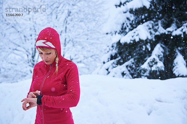 Läuferin in roter Kapuze kontrolliert Smartwatch im Schnee,  Gstaad,  Schweiz