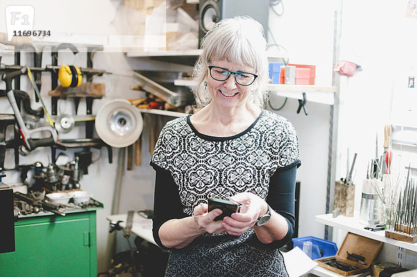 Lächelnde Seniorin mit Handy in der Schmuckwerkstatt
