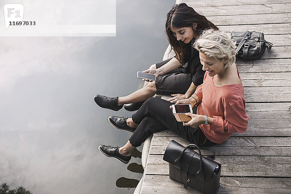 Großer Blickwinkel auf glückliche Geschäftsfrauen mit dem Smartphone auf dem Pier am See