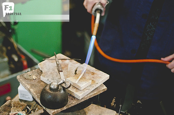 Mittelteil eines älteren Handwerkers,  der eine Lötlampe für die Metallbearbeitung in der Schmuckwerkstatt einsetzt