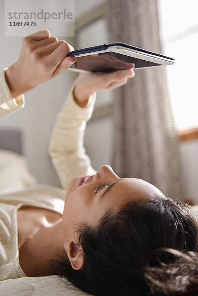 Hispanische Frau liegt auf dem Bett und liest auf einem digitalen Tablet