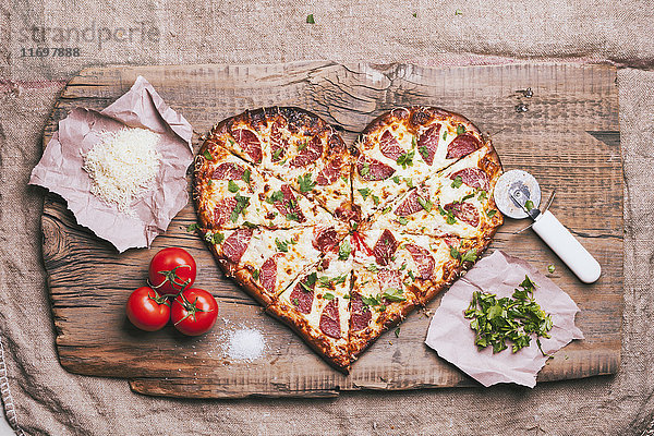 Herzförmige Pizza und Zutaten auf dem Schneidebrett