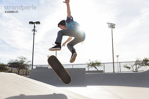 Hispanischer Mann,  der einen Trick in der Luft auf einem Skateboard vorführt