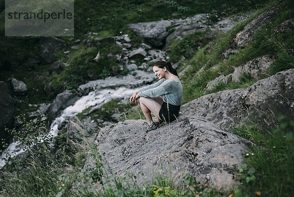 Lächelnde kaukasische Frau sitzt auf einem Felsen auf einem Hügel