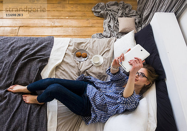 Kaukasische Frau,  die auf dem Bett liegt und für ein Selfie mit einem digitalen Tablet posiert