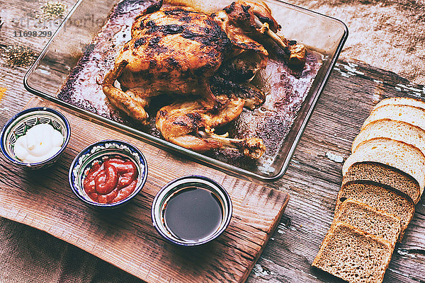 Nahaufnahme von gebratenem Huhn mit Brot und Soßen auf Holztisch