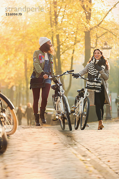 Junge Frauen,  die mit dem Fahrrad durch die sonnige Herbststraße laufen.