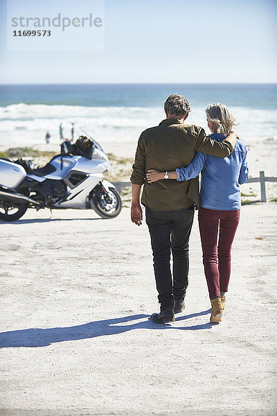 Liebevolles Seniorenpaar,  das am sonnigen Strand zum Motorrad läuft