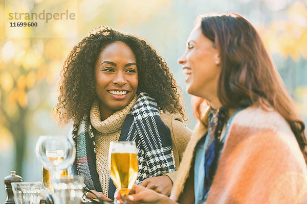 Lächelnde junge Frauen Freunde trinken Bier im Herbst Bürgersteig Cafe