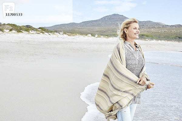 Reife Frau genießt das Meer,  eingehüllt in eine Decke