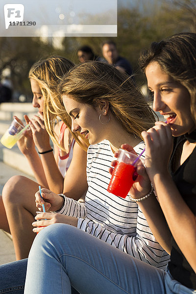Drei junge Frauen mit Erfrischungsgetränken bei Sonnenuntergang