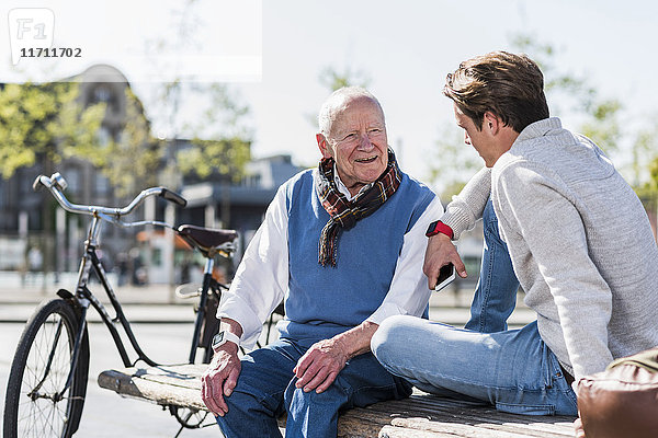 Senior und erwachsener Enkel im Gespräch auf einer Bank