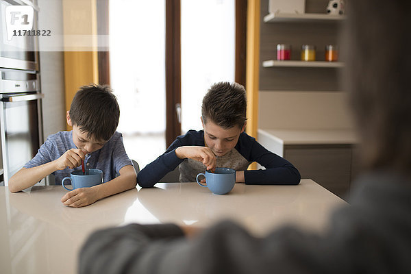 Zwei Jungen essen Seite an Seite am Küchentisch.