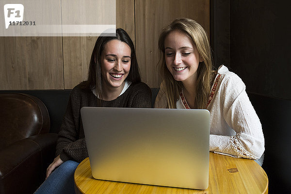 Zwei lächelnde Freunde,  die in einem Café sitzen und auf den Laptop schauen.