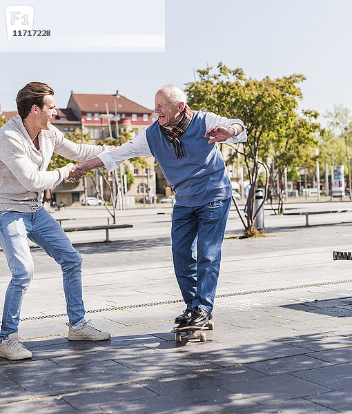 Erwachsener Enkel,  der dem älteren Mann auf dem Skateboard assistiert.