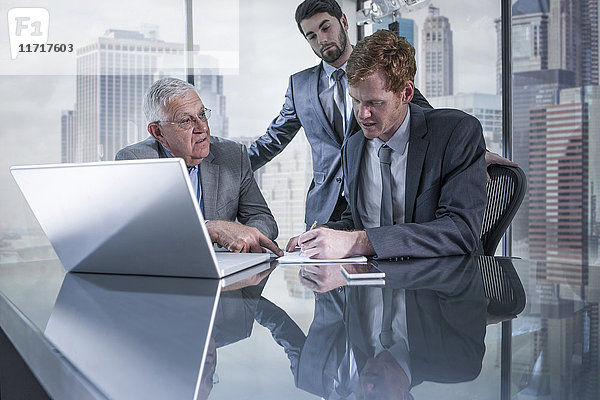 Drei Geschäftsleute mit Laptop diskutieren im Büro
