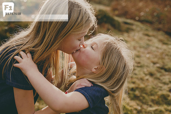 Zwei süße blonde Schwestern,  die sich draußen küssen.