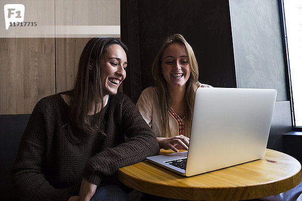 Zwei glückliche Freunde,  die in einem Café sitzen und auf den Laptop schauen.