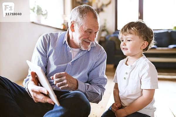 Großvater und Enkel auf dem Boden sitzend,  mit digitalem Tablett