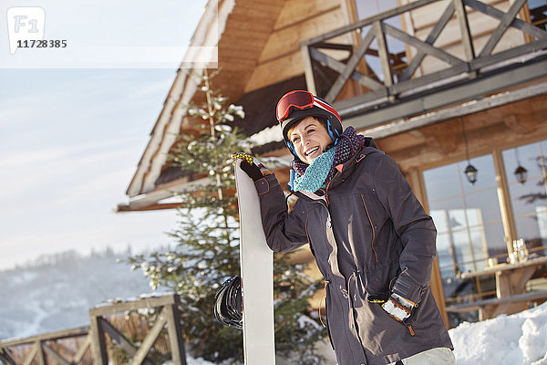 Lächelnde Snowboarderin mit Snowboard außerhalb der sonnigen Hütte