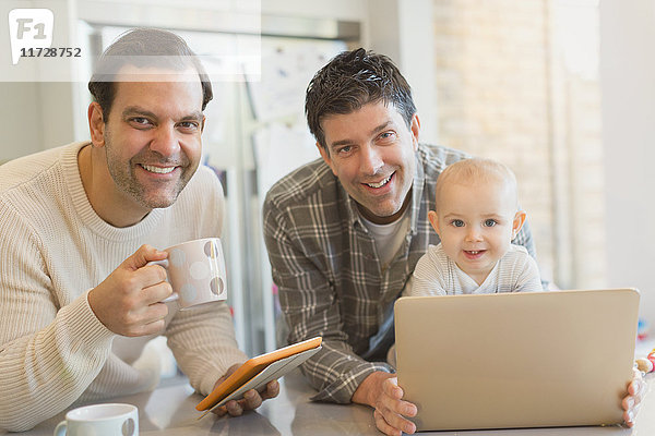 Portrait lächelnden männlichen schwulen Eltern mit Baby-Sohn mit digitalen Tablett und Laptop in der Küche
