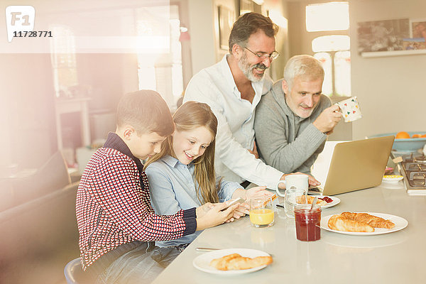 Schwule Eltern und Kinder mit Laptop und Handy,  Frühstücken in der Küche
