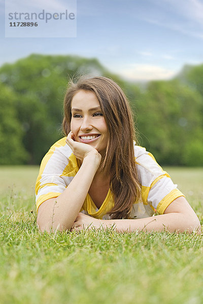 Porträt einer brünetten Frau im Park liegend,  lächelnd und nachdenklich