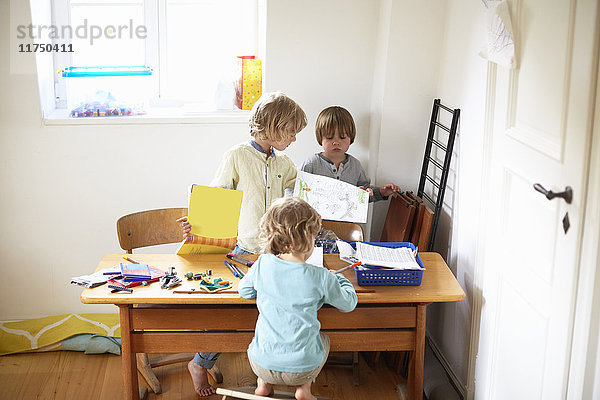 Drei Jungen sitzen am Tisch und zeichnen Bilder