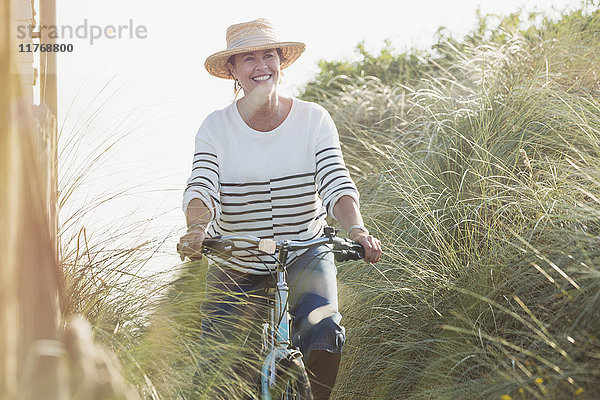 Lächelnde reife Frau beim Fahrradfahren entlang des Strandgrases