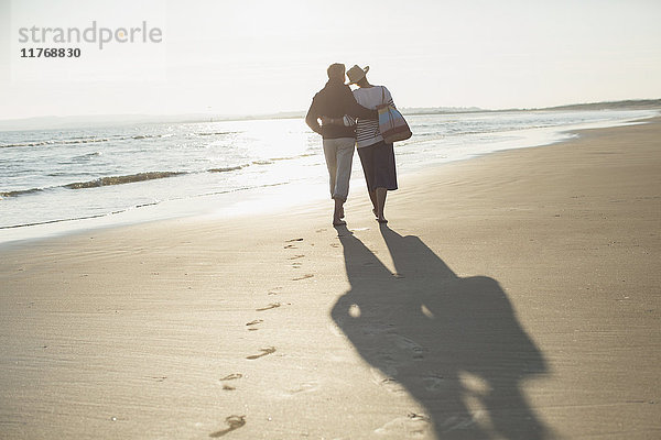 Zärtliches,  reifes Paar,  das sich umarmt und am sonnigen Strand spazieren geht.