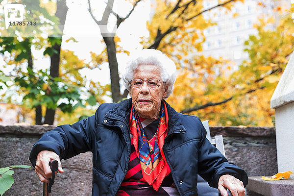 Porträt einer selbstbewussten Seniorin,  die im Herbst im Park sitzt.