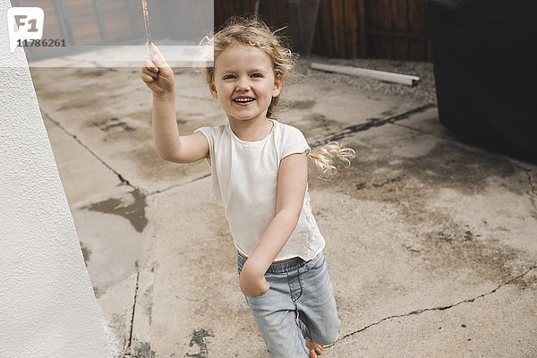 Porträt eines glücklichen Mädchens beim Spielen mit dem Zauberstab vor dem Haus