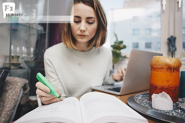 Frau studiert mit Laptop und Buch am Tisch im Studentenwohnheim