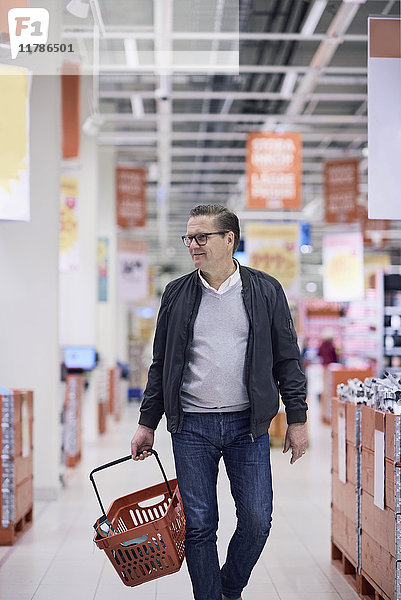 Lächelnder Mann mit Korb beim Gehen im Supermarkt