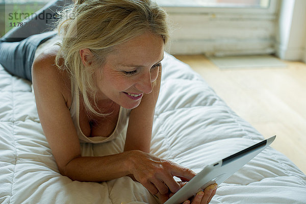 Reife Frau entspannt auf dem Bett mit digitalem Tablett