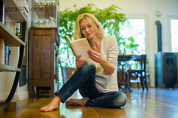 Reife Frau entspannt auf dem Boden mit Buch zu Hause