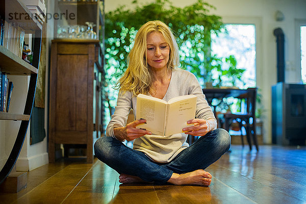 Reife Frau sitzt zu Hause auf dem Boden,  liest Buch